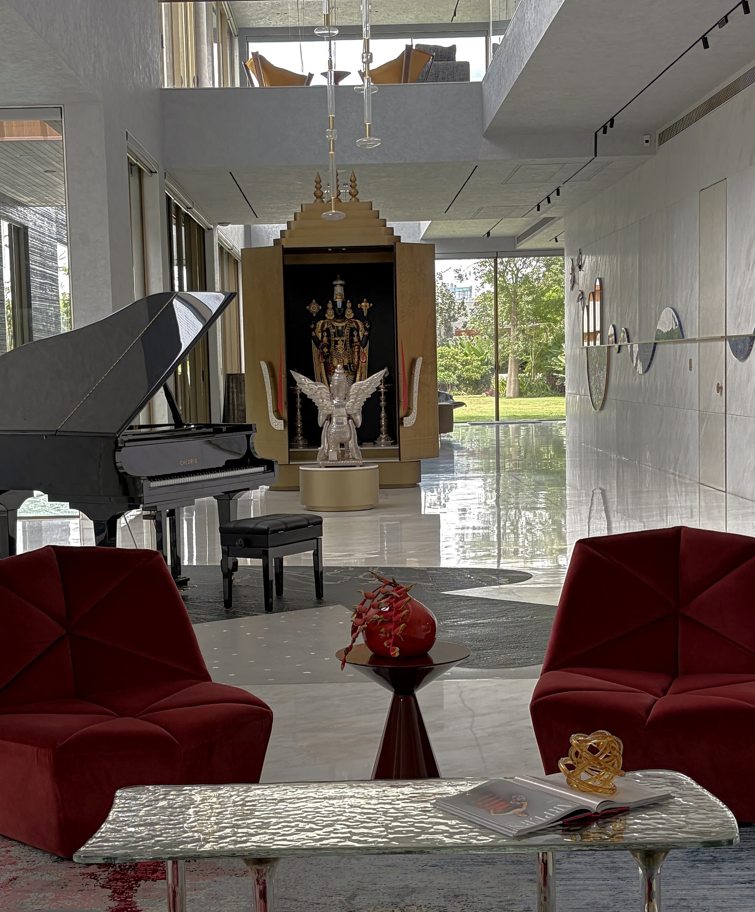 Hall vignette: burgundy velvet chairs and a hammered-glass table before the piano and the gilded shrine.