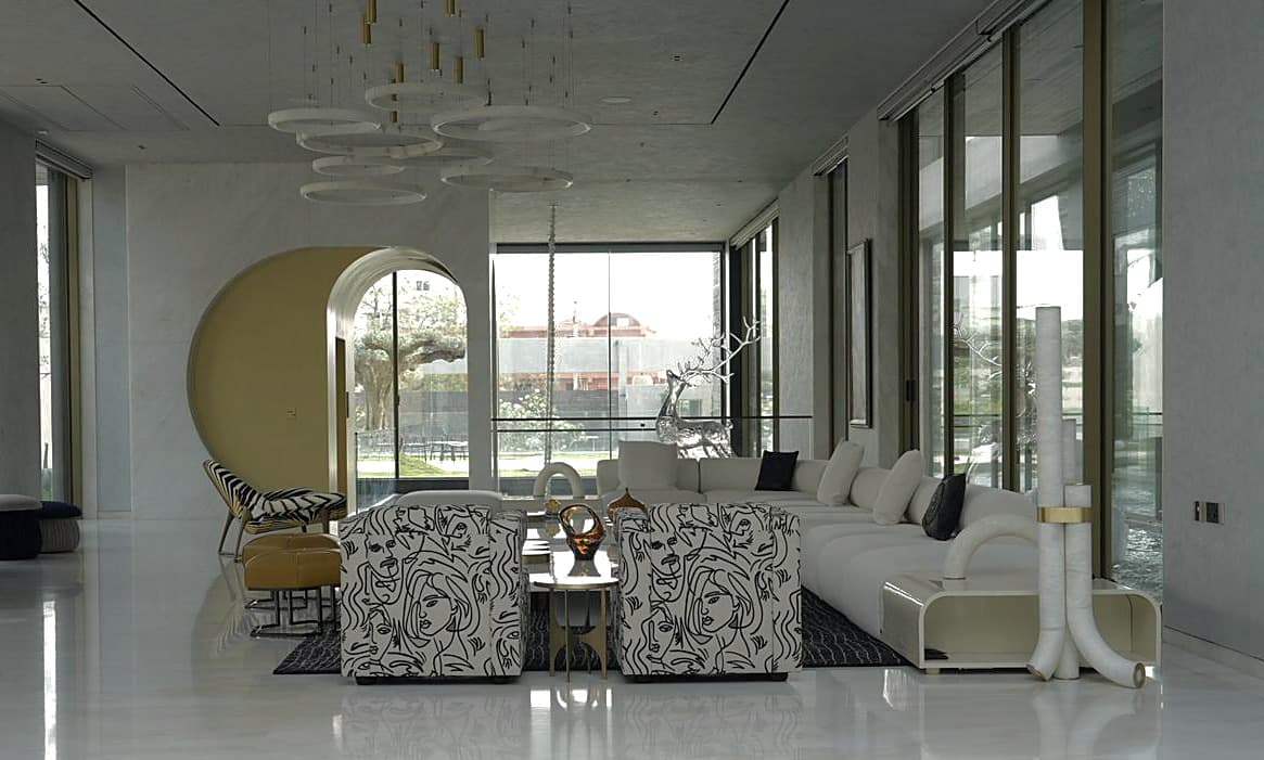 Formal lounge: line-drawn armchairs and cream sofa beneath alabaster rings, gilded arch and zebra chair beyond.