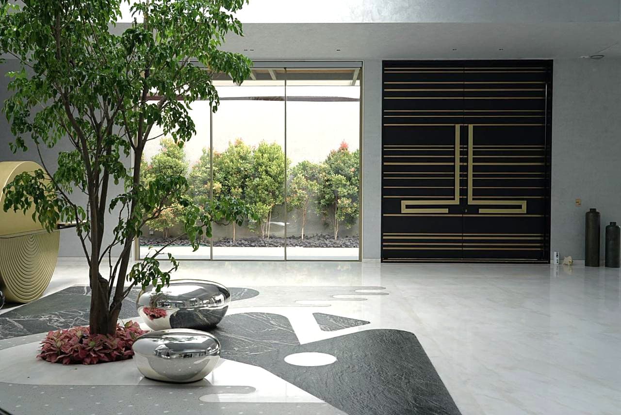 Entry hall: brass-inlaid black doors, the courtyard tree over mirror-polished pebbles and the inlaid stone floor.