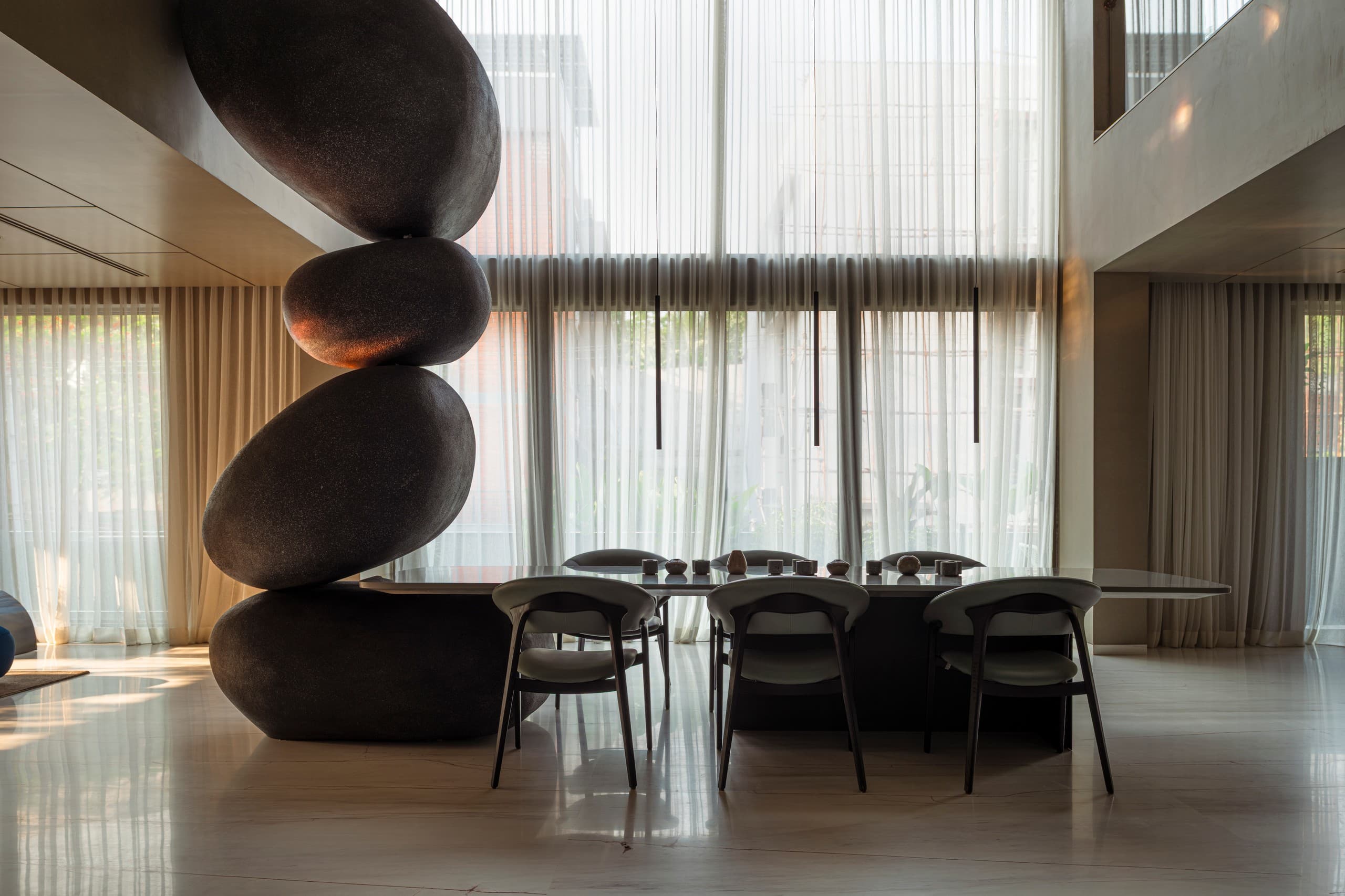 Double-height dining room with a column of stacked stone forms beside the table.