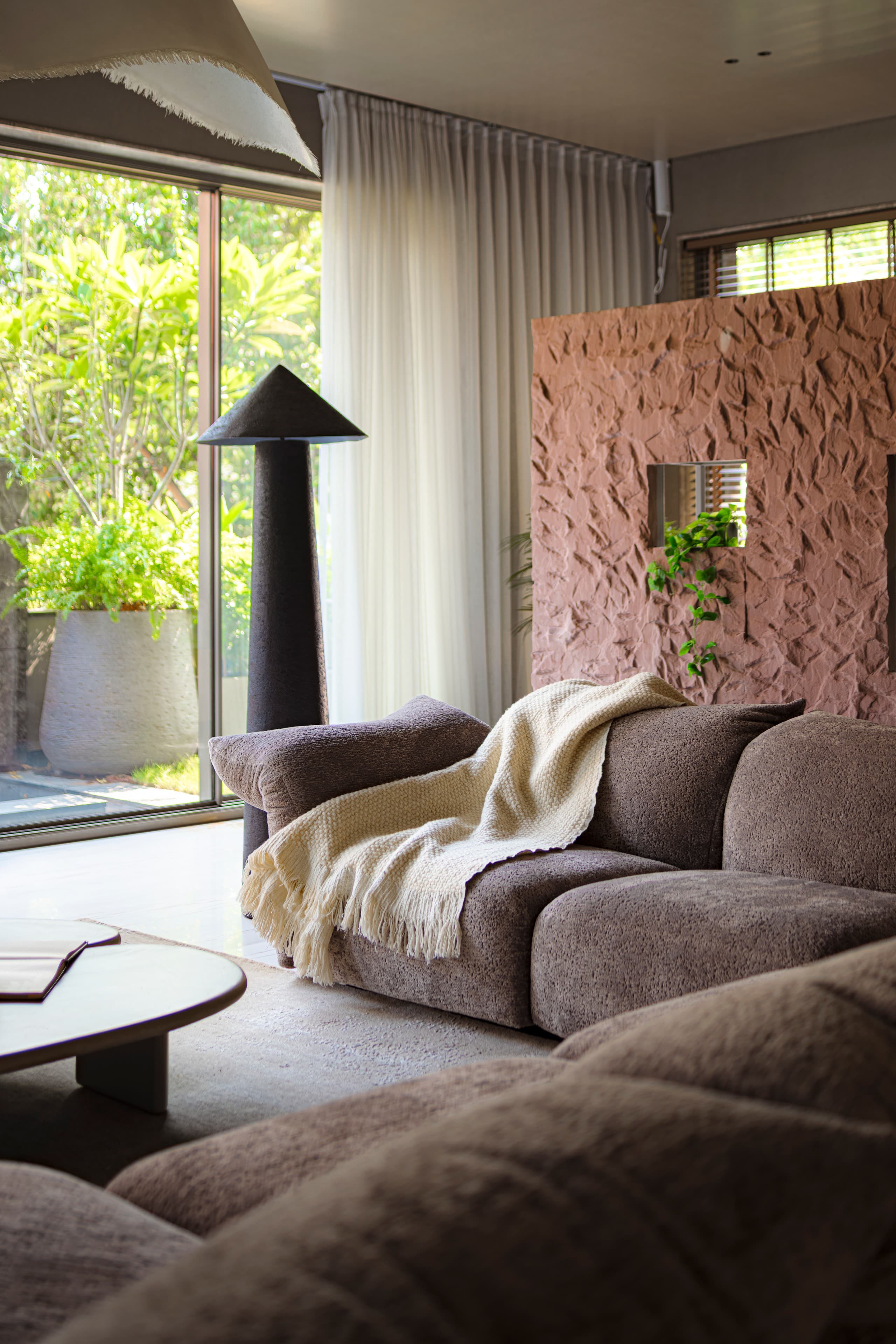 Bouclé armchair against hand-textured pink plaster with a dark cone lamp.