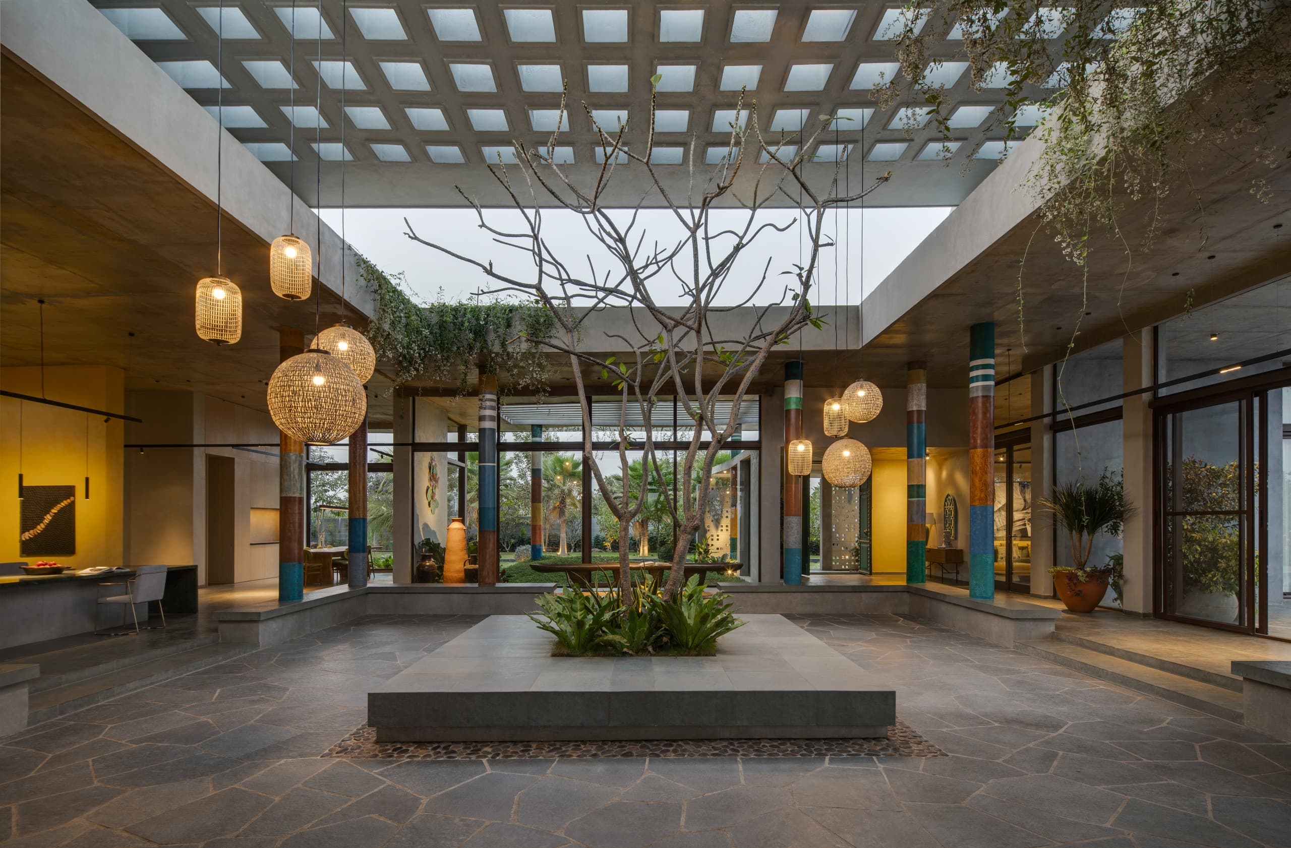 The courtyard canopy at evening, woven pendants lit among the tree.
